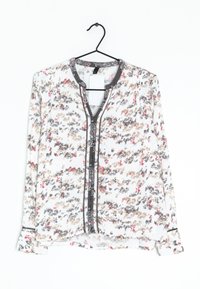 Blusa bianca con motivo floreale nei colori rosa, marrone e nero. Presenta una chiusura frontale con bottoni, scollatura rotonda e maniche lunghe. Tessuto texturizzato.