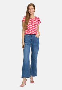 Lyserød mønstret bluse med korte ærmer, parret med brede blå denimjeans og lyserøde hæle, der fremhæver en afslappet pasform og afslappet stil.