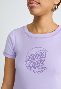 Lilac short-sleeve t-shirt featuring raised purple graphic text "SANTA CRUZ" with wavy accents, cotton material, and a fitted design.