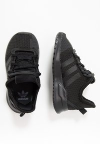 Svarta träningsskor med mesh-överdel, texturerade detaljer och ett mönster med tre ränder. Har en vadderad krage och gummisula för grepp.