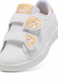 Fehér sneaker tépőzáras pántokkal, világos narancssárga és ezüst díszítésekkel. Sim felületű szintetikus anyag, kerek orr és párnázott nyak.