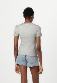 Pelēks pieguļošs īsām piedurknēm tops ribu tekstūrā, ar apaļu kakla izgriezumu un kontrastējošiem šuvēm, kombinēts ar gaiši ziliem džinsu šortiem.