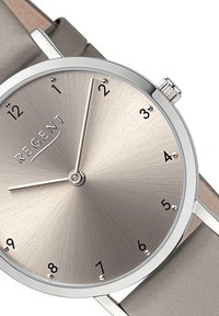 Montre en métal argenté avec un cadran argenté brossé. Son design minimaliste présente des index horaires noirs et un bracelet en cuir gris lisse.