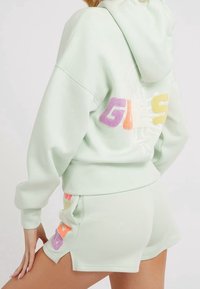 Ljusgrön hoodie och shorts-set, med en texturerad, flerfärgad "GUESS"-logotyp på baksidan och sidan. Mjuk material med en avslappnad passform.