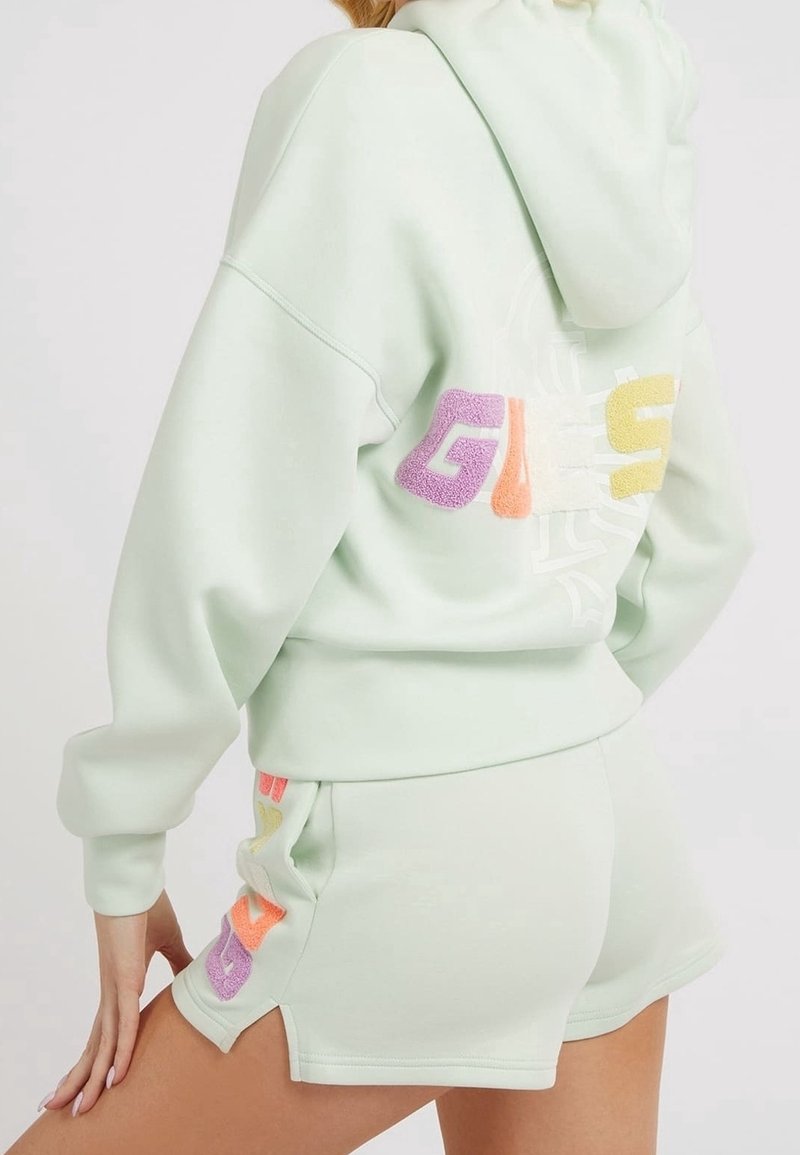 Ljusgrön hoodie och shorts-set, med en texturerad, flerfärgad "GUESS"-logotyp på baksidan och sidan. Mjuk material med en avslappnad passform.