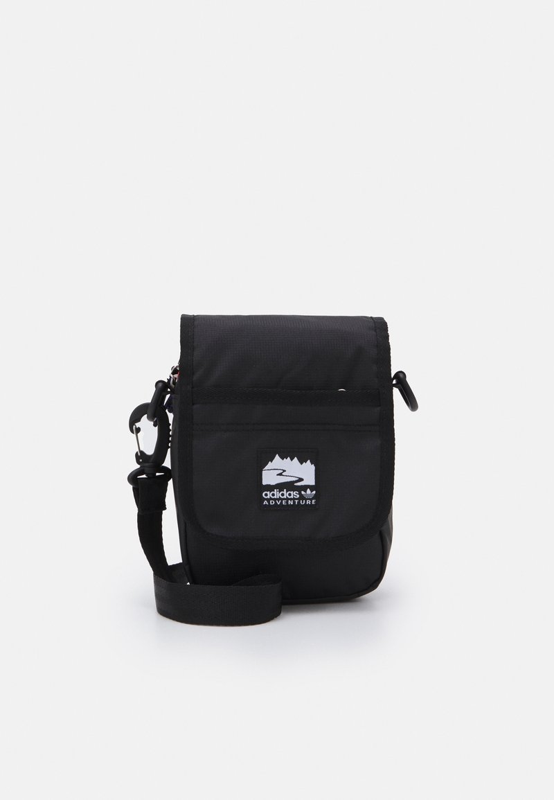 Black nylon crossbody bag with a flap closure, adjustable strap, front logo patch, and two external clips for attachment.
