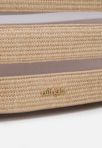 Luonnollinen kudottu olkalaukku, jossa on teksturoitu pinta, vaaleanbeige väri, ruskeat kangasraidat ja kullanvärinen logoyksityiskohta.