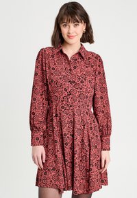 Robe à boutons en tissu rouge avec un motif floral noir, manches longues, corsage ajusté et jupe évasée avec des détails de plis.