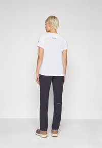 White short-sleeve athletic shirt with a logo on the back, paired with dark gray hiking pants. Shoes are light brown with accents.