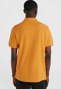 Polo de manga corta en naranja brillante, hecho de tejido texturizado. Presenta un collar clásico y aberturas laterales en el dobladillo para facilitar el movimiento.