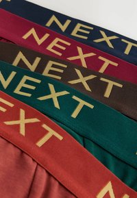Quatre bandes de tissu en bordeaux, marine, vert foncé et marron, chacune portant le mot « NEXT » en lettres dorées sur une surface texturée.