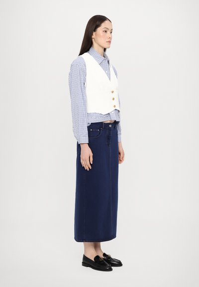 Hvit vest over en blå rutete skjorte, parret med et langt marineblått denimskjørt og svarte loafers med en dekorativ aksent.