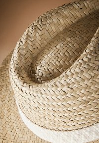 Chapeau de paille à large bord, tissé en matériau beige clair. Présente une bande douce et texturée autour de la base de la calotte.