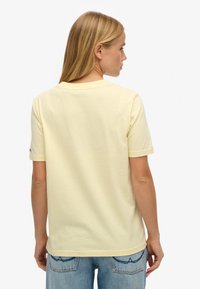 Gul bomulds t-shirt med rund halsudskæring og korte ærmer, vist fra ryggen, båret med lyseblå denimjeans.