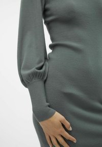 Abito lavorato a maglia in un morbido tono di verde tenue. Presenta maniche lunghe e svasate con polsini a costa e una silhouette aderente che mette in risalto una texture liscia.