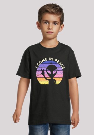 Schwarzes Baumwoll-T-Shirt mit einer Cartoon-Aliensgrafik und dem Text "ICH KOMME IM FRIEDEN", vor einem gradienten gestreiften Hintergrund.