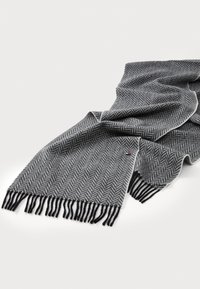 Écharpe en motif chevrons gris avec des bords frangés et une bordure blanche contrastante, fabriquée en tissu doux. Présente un petit accent de logo.