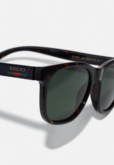 Ochelari de soare Gucci cu un cadru din marmură, lentile verzi și accente cu logo auriu. Au o formă rectangulară clasică și o textură netedă.