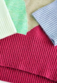 Pletací látkové vzorky v pastelových barvách: světle zelená, růžová, krémově žlutá a světle modrá, s ribovanými a hladkými texturami a výraznými tvary.