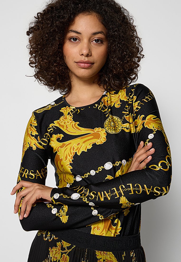 Haut noir à manches longues avec un motif baroque jaune et des accents blancs. Fabriqué en tissu lisse, il a une silhouette ajustée et un col rond.