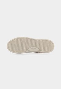 Semelle de chaussure en caoutchouc beige avec petit motif en losanges et logo "ALDO" embossé près de la zone de la voûte plantaire, à plat sur fond blanc.