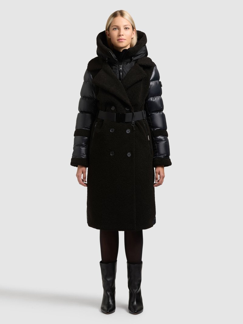 Fekete, két anyagból álló kabát párnázott felsőrészzel és gyapjúszerű alsó résszel, övvel, túlméretezett gallérral és hosszú ujjakkal.