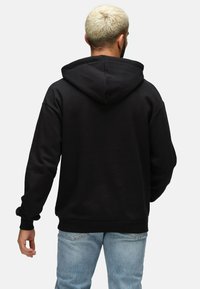 Sudadera con capucha negra de textura, con un bolsillo tipo canguro y puños de canalé, combinada con jeans de un azul claro.