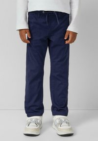 Pantalon en coton bleu marine avec un waistband à cordon, design à jambe droite et détails de couture minimaux, associé à des baskets blanches et grises.