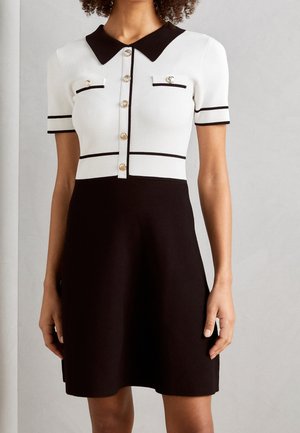 Vestido en blanco y negro con mangas cortas, cuello con solapa, botones dorados y dos bolsillos en el pecho con detalles en negro.