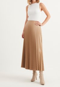 Beige plisserad kjol med en slät, glänsande yta, matchad med en vit ribbad linne och knähöga beige stövlar.