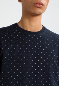 Maglione di cotone blu navy con scollo a girocollo, caratterizzato da un motivo di punti bianchi sparsi. Texture morbida e design aderente.