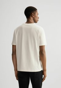 Helles Cremefarbenes T-Shirt mit kurzen Ärmeln aus weichem Baumwollstoff, ausgestattet mit einem klassischen Rundhalsausschnitt und einer lockeren Passform, mit einer glatten Textur.