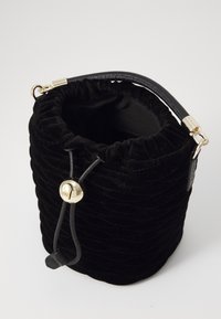 Sac en velours noir à cordon de serrage, de forme arrondie, avec une fermeture en métal doré en forme de cloche et une surface texturée. Sangle en cuir incluse.