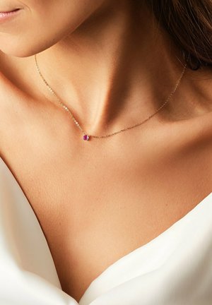 Gold chain necklace with a small round purple gemstone pendant, resting on bare skin. Simple design with a delicate appearance.