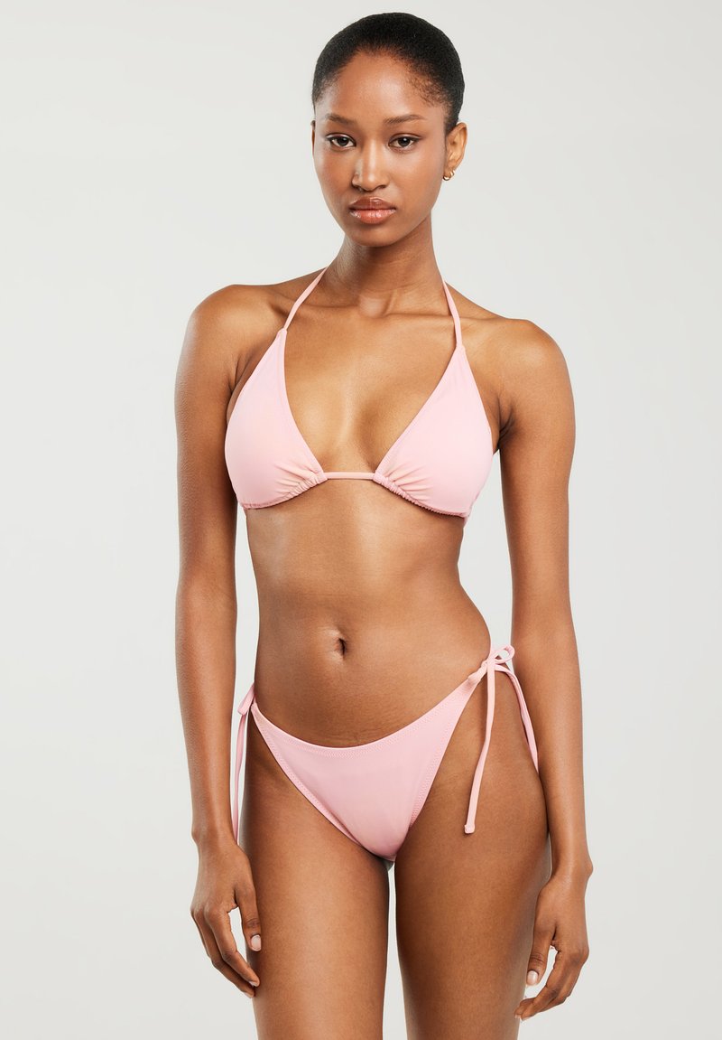 Różowy strój kąpielowy składający się z trójkątnego stanika z regulowanymi wiązaniami oraz dopasowanych, niskich majtek z wiązaniami po bokach. Gładki, elastyczny materiał.
