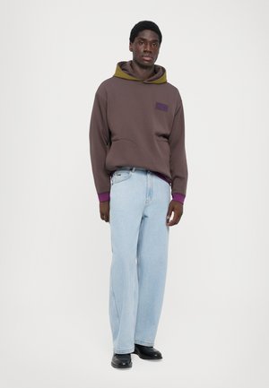 Brown hooded sweatshirt with a purple pocket and olive green lining, paired with light blue wide-leg jeans and black shoes.