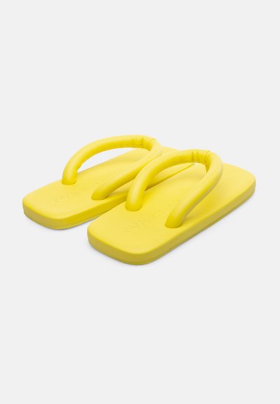 Des tongs jaunes en caoutchouc souple et durable, avec des sangles rembourrées et une semelle plate, présentant une texture lisse et des bords arrondis.