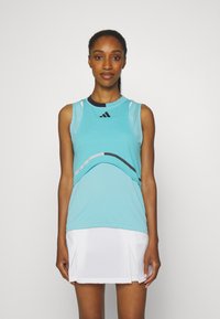 Een turquoise sporttanktop met zwarte accenten, voorzien van een ronde halslijn en meshpanelen. Gecombineerd met een witte geplooide rok.