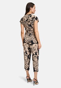 Combinaison florale avec une base noire et des motifs tropicaux beiges. Manches courtes, taille cintrée et jambes raccourcies. Assortie à des sandales à talons hauts.