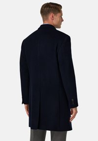 Námořnický vlněný kabát s dlouhým střihem, s vykrojeným límcem a jediným rozparkem. Obsahuje manžety na čtyři knoflíky a hladkou strukturu.