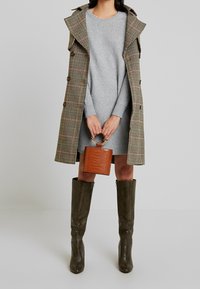 Grå stickad klänning ihopsatt med en houndstooth-kappa, brun handväska med krokodilsmönster och knähöga olivgröna läderstövlar.