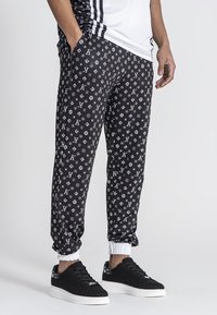 Zwarte sport joggers met een herhalend wit logopatroon, elastische tailleband en boorden. Gecombineerd met zwarte sneakers.