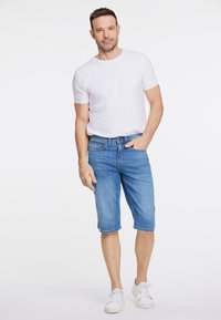 Niebieskie dżinsowe szorty o prostym kroju, z przednimi kieszeniami i delikatnym przetarciem na dolnym brzegu, zestawione z gładką białą koszulką i białymi trampkami.