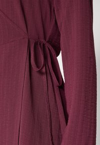 Djuplila tyg med subtila vertikala ränder, med ett knytbart midjebälte och långa ärmar på ett plagg.