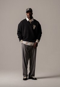 Hanorac negru cu detalii de logo, cămașă albă cu guler, pantaloni gri și pantofi negri cu accente albe. Look casual streetwear.