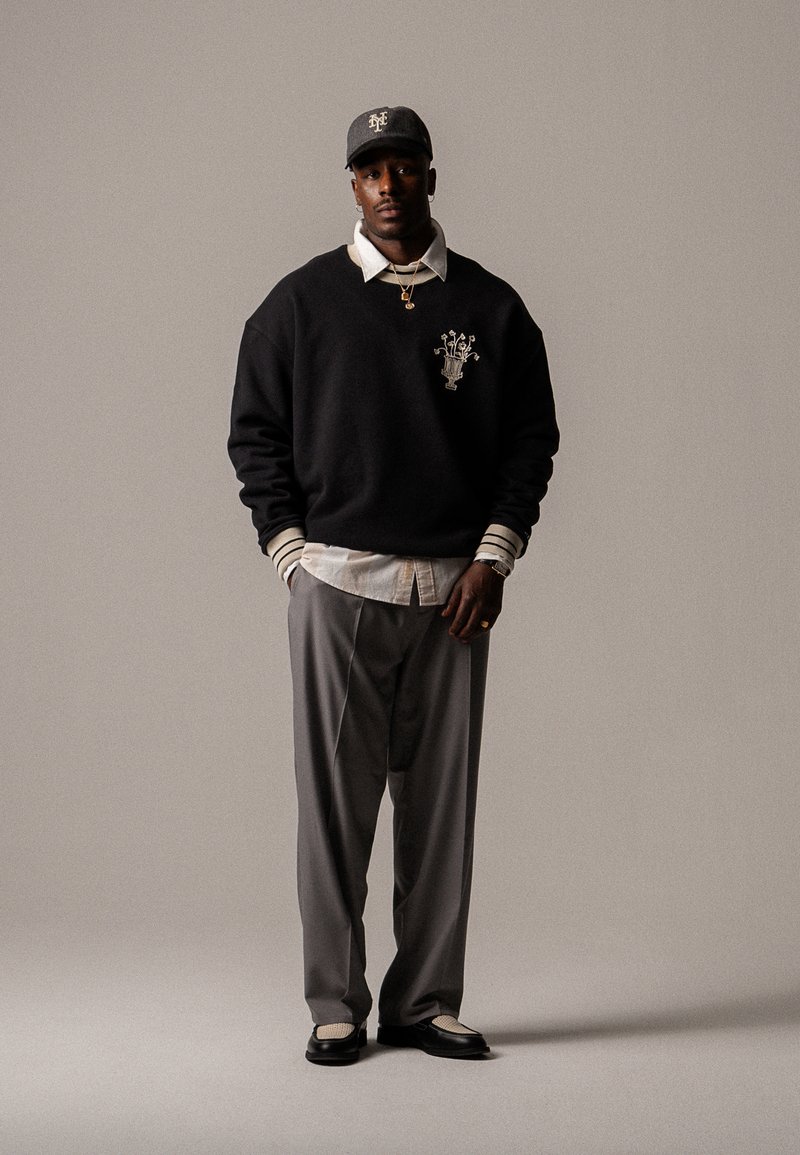 Hanorac negru cu detalii de logo, cămașă albă cu guler, pantaloni gri și pantofi negri cu accente albe. Look casual streetwear.