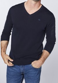 Marinblå v-ringad tröja i stickad tyg med lång ärm och ribbade muddar och nederkant; har en liten logotyp på bröstet.