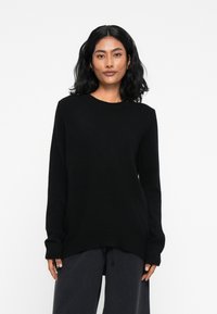Sweater preto de malha com mangas longas, decote redondo e corte descontraído. Textura suave com punhos e barra canelados.