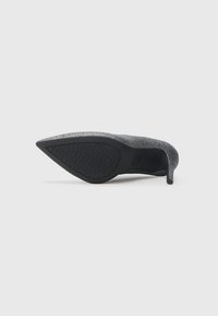Black high-heeled shoe with a textured surface and pointed toe. Features a slim stiletto heel and a patterned rubber sole for grip.