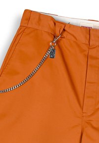 Pantalones naranjas con una textura suave, que presentan un acento de cadena lateral, herrajes de metal y un cierre de cremallera.